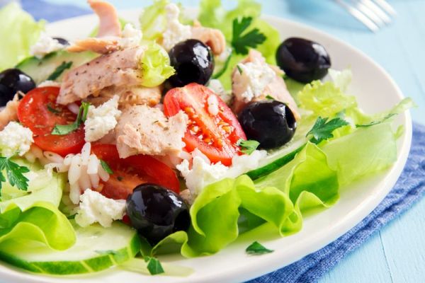 Tuna salad with tomatoes, black olives, rice, feta cheesse and greens close up