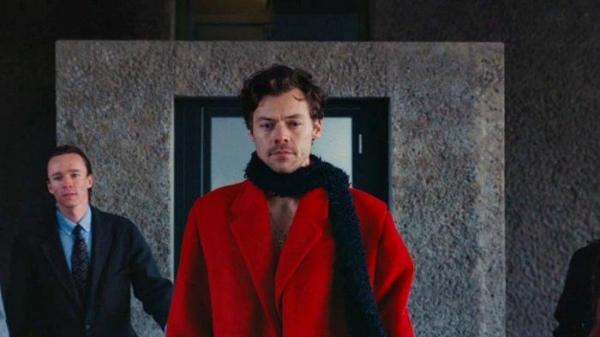 Harry Styles mengenakan mantel berwarna merah terang, lengkap dengan aksesoris syal bulu berwarna hitam di video klip single terbarunya 