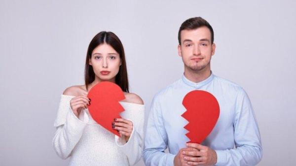 Guy and girl holding two pieces of broken heart on white background