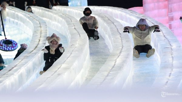 Foto yang diambil pada 21 Desember 2024 ini menunjukkan pengunjung bermain di seluncuran es di Festival Dunia Es dan Salju Harbin di Harbin, provinsi Heilongjiang, Tiongkok timur laut. - Festival tahunan edisi ke-26 secara resmi dibuka pada tanggal 21 Desember di Harbin, yang juga dikenal sebagai 