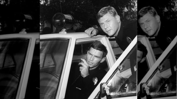 Actor Martin Milner leans over the door of a patrol car as Kent McCord talks on the police radio in a promotional still for the television series, 'Adam 12,' c. 1969.
