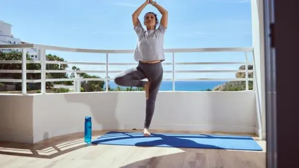 Young yogi woman practicing yoga concept, sitting in paschimottanasana exercise, using wooden block, seated forward bend pose, wearing black sportswear, working out, full length, white loft background