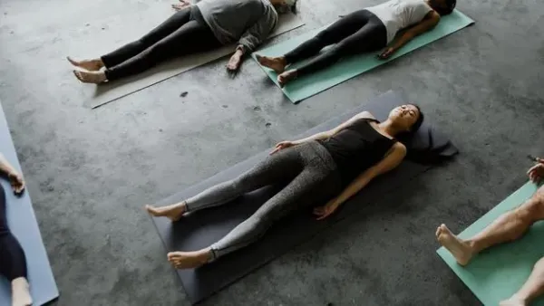 Young yogi woman practicing yoga concept, sitting in paschimottanasana exercise, using wooden block, seated forward bend pose, wearing black sportswear, working out, full length, white loft background