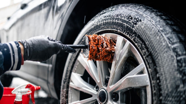 A person wearing black gloves using a brush to clean vehicle rims.