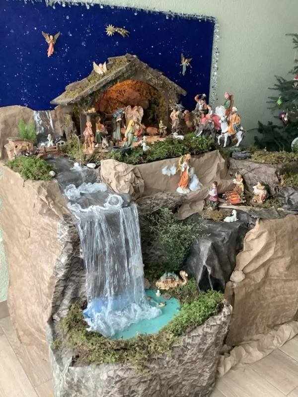 This may contain: a nativity scene is displayed on the wall next to a christmas tree and small waterfall