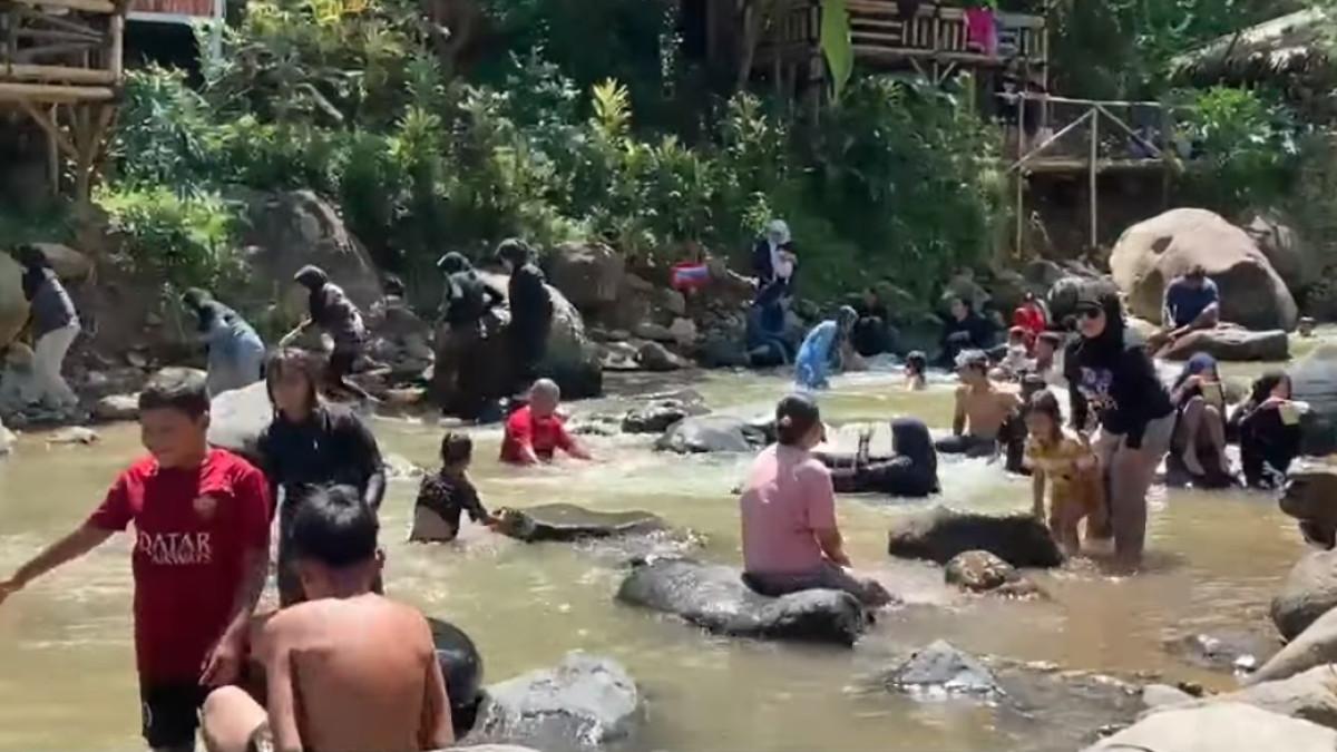 Pengunjung menikmati aliran sungai yang tenang di bawah Curug Leuwi Kunten, cocok untuk keluarga.