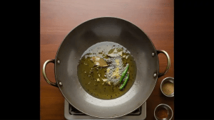 Oil is heated in a pan and mustard seeds, asafoetida, bay leaves, ginger, and green chilies are added to release aroma.