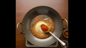 Red chili powder and turmeric are added to the pan and stirred quickly so the spices do not burn.