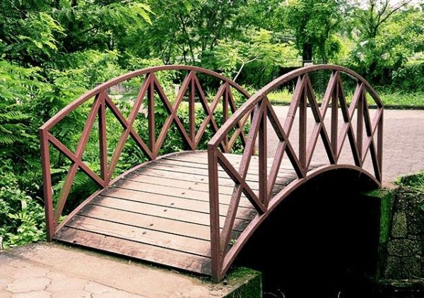 This may contain: a wooden bridge over a small stream in a park with lots of trees and bushes