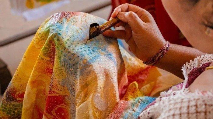 Ilustrasi tangan yang sedang membuat motif kain batik menggunakan canting