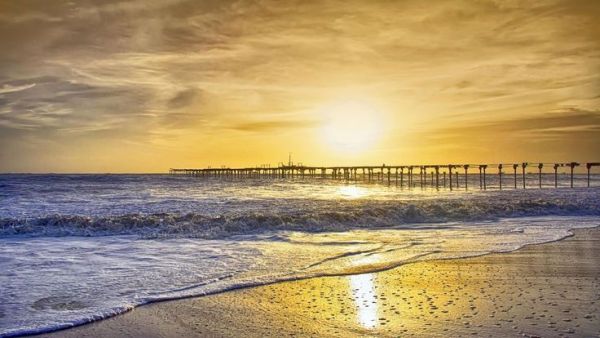 This may contain: the sun is setting over the ocean with waves coming in to shore and a pier stretching out into the distance