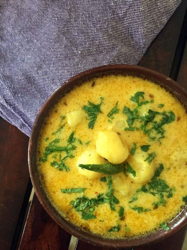 This may contain: a brown bowl filled with food on top of a wooden table next to a napkin