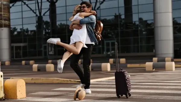 A delighted man is surprised by his partner at the airport, lifting her into a tight embrace. 