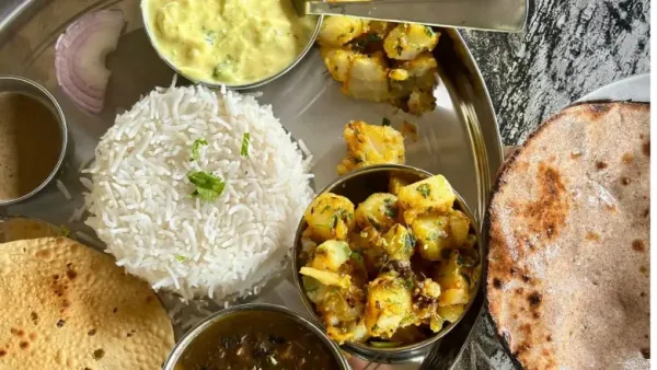 A vibrant, close-up overhead shot of a traditional Indian thali meal served on a round, silver metal plate.