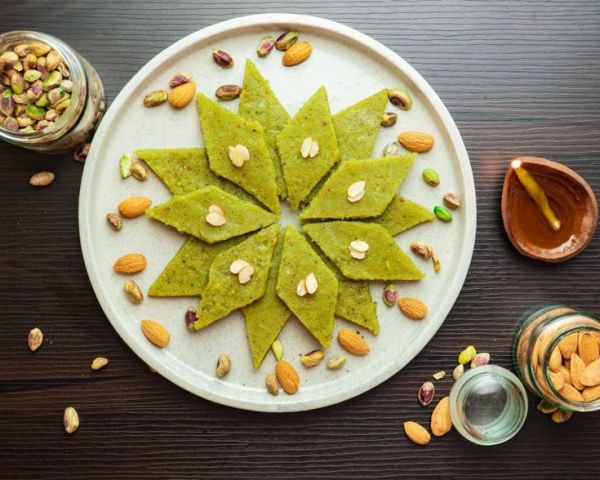 This may contain: a white plate topped with green pancakes covered in almonds and pistachio seeds