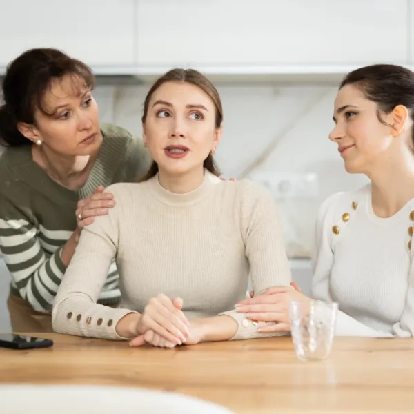 two women touching friend sitting at table