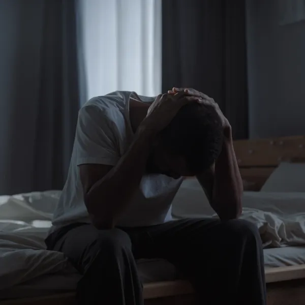 depressed man sitting in dark bedroom holding head in hands