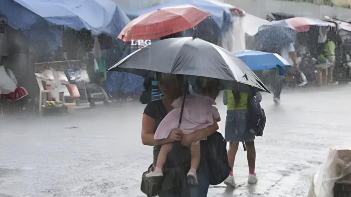 HUJAN SIANG- Seorang wanita menggendong anaknya di tengah kondisi cuaca hujan siang hari.