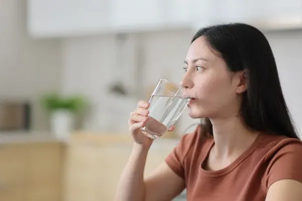 Asian woman drinking tap water from glass in the kitchen
