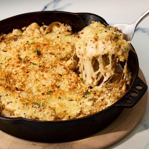 Cheesy baked dish with a crispy topping in a skillet a serving spoon lifting a portion Credit: Photographer: Victor Protasio, Food Stylist: Chelsea Zimmer, Prop Stylist: Prissy Lee.