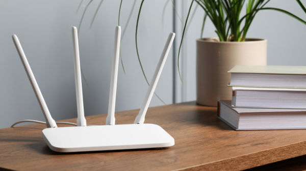 white router with four antennas placed on a wooden table alongside books and a plant