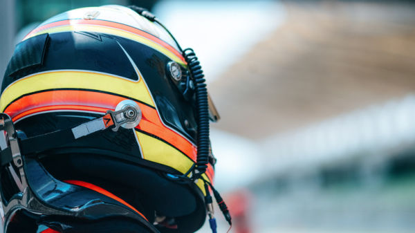 Driver wearing generic racing helmet with radio wire running on the right-side, rear-right view