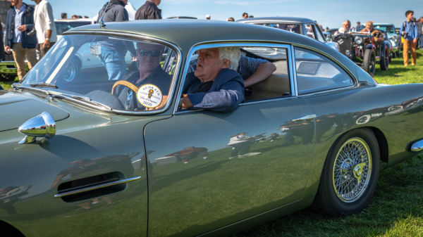 Jay Leno sitting in an Aston Martin at an Audrain Concours event.
