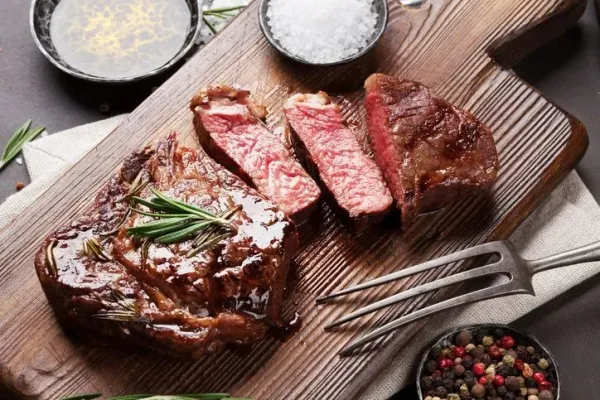 Sliced medium rare grilled Steak Ribeye with french fries on serving board block on wooden background