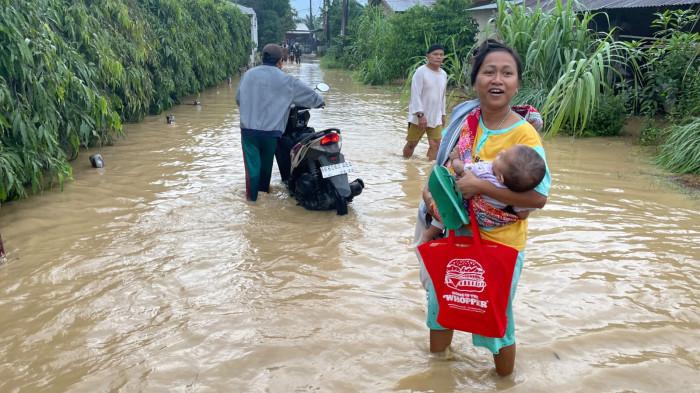 BANJIR- Seorang ibu menggendong bayinya di tengah kondisi banjir di Desa Dalu X B Kecamatan Tanjung Morawa, Deli Serdang, Kamis (29/10/2026). Saat ini banjir melanda 16 Desa di 8 Kecamatan.